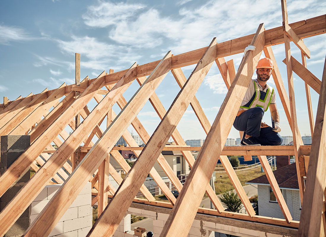 Insurance by Industry - View of a Male Contractor Standing on the Wood Framing on the Roof of a New Residential Building Project on a Sunny Day